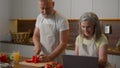 Caucasian retired couple in chefs aprons smiling cooking at home kitchen middle-aged woman wife using laptop culinary Royalty Free Stock Photo