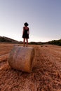 Caucasian 30s brunette woman, standing on a hay bale during Golden hour