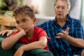 Caucasian sad boy with hand on chin looking away while sitting with grandfather on sofa