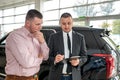 Caucasian salesman holding clipboard and talking about buying car with sale with his customer Royalty Free Stock Photo