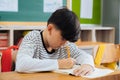 Caucasian school boy sitting in school writing in book with pencil, studying, education, learning. Male student sitting
