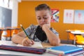 Caucasian schoolboy with face mask sitting in classroom concentrating and writing in schoolbook