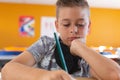 Caucasian schoolboy with face mask sitting in classroom concentrating and writing in schoolbook