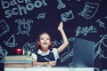 Caucasian schoolgirl raises hand up sits at laptop during online lesson. Distant School Learning. Royalty Free Stock Photo