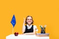 Caucasian schoolgirl raising hand sitting at the desk during lesson. English lesson. Europe flag