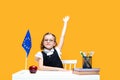 Caucasian schoolgirl raising hand up sitting at the desk during lesson. English lesson. Europe flag