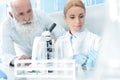Caucasian scientists in uniform working with microscope and flasks in chemical laboratory Royalty Free Stock Photo