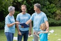 Caucasian senior couple with clipboard and man and son in volunteer shirts talking in littered field