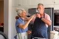 Caucasian senior couple standing in kitchen, drinking wine and preparing meal together Royalty Free Stock Photo