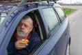 Caucasian senior driver eating patty with apple inside his car on short stop on roadside while traveling