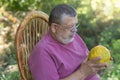 Caucasian senior farmer sitting in whicker chair and watching on ripe melon in hands Royalty Free Stock Photo