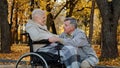 Caucasian senior man holding female hand caring woman with disability on wheelchair husband accompanies sick wife during Royalty Free Stock Photo