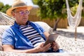 Caucasian senior man wearing hat using digital tablet while resting on hammock at beach Royalty Free Stock Photo