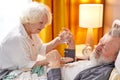 Caucasian Senior man taking medicines and drinking water while lie on bed, wife help and support Royalty Free Stock Photo