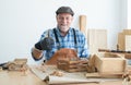 Caucasian senior old bearded man carpenter in apron, hat and gloves sitting smiling, thumbs up, working in workshop, tools machine Royalty Free Stock Photo