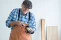 Caucasian senior old white bearded man carpenter in apron, gloves and hat using chisel working in workshop, smiling, standing in Royalty Free Stock Photo