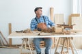 Caucasian senior old white bearded man carpenter in apron, hat and gloves working in workshop, thinking looking out of window, Royalty Free Stock Photo