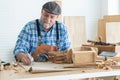 Caucasian senior old white bearded man carpenter in apron, hat and gloves working in workshop, use pencil sketching a design on Royalty Free Stock Photo