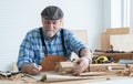 Caucasian senior old white bearded man carpenter in apron and hat working in workshop, sketching a car model design on paper, Royalty Free Stock Photo