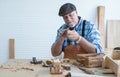 Caucasian senior old white bearded man carpenter in apron and hat working in workshop, use sandpaper polishing handmade wood toy, Royalty Free Stock Photo