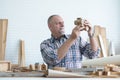 Caucasian senior old white bearded man carpenter working in workshop, holding, looking at handmade wood car toy in detail, tools Royalty Free Stock Photo