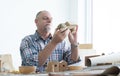 Caucasian senior old white bearded man carpenter working in workshop, holding, looking at handmade wood car toy in detail, tools Royalty Free Stock Photo