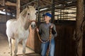 Senior woman horse breeder standing with white horse in barn Royalty Free Stock Photo