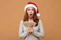 Caucasian shocked lady wearing christmas hat holding money.