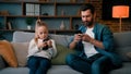 Caucasian single daddy and child kid preschooler girl sit on sofa look at mobile phone screen chatting online use home
