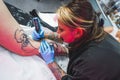 Caucasian tattooist girl working on a leg, medium closeup shot, tattoo studio