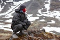 Caucasian teenage boy dressing warm hiking outfit for mountaineering, young man sitting on big stone and looking far away in Royalty Free Stock Photo