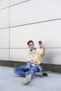 Caucasian teenage boy sitting on a skateboard taking a picture of himself with a mobile phone. Urban lifestyle Royalty Free Stock Photo