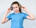 Caucasian teenage girl listening music with wireless headphones, blue t-shirt, a grey background Royalty Free Stock Photo