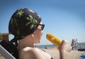 A Caucasian teenager boy in a bandana and sun glasses eats boiled corn on the beach . The concept of relaxation and tranquility.