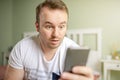 Caucasian white young man looking shocked at his phone with big opend eyes. Royalty Free Stock Photo