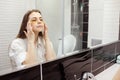 Caucasian woman applying hydrogel patches on under eye area, looking at mirror. Happy young lady enjoying morning anti Royalty Free Stock Photo