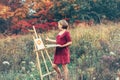 Caucasian woman artist drawing in open plein air outside autumn fall with watercolor on paper at easel.