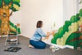 Caucasian woman artist hand painting murals on walls indoor at an apartment or a studio school with acrylic paints. Lifestyle Royalty Free Stock Photo