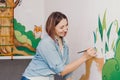 Caucasian woman artist hand painting murals on walls indoor at an apartment or a studio school with acrylic paints. Lifestyle Royalty Free Stock Photo