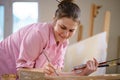 Caucasian woman artist working on a painting in bright daylight studio. Happy artist draws an art project with paints