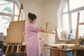 Caucasian woman artist working on a painting in bright daylight studio. Happy artist draws an art project with paints