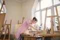 Caucasian woman artist working on a painting in bright daylight studio. Happy artist draws an art project with paints Royalty Free Stock Photo