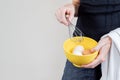 Caucasian woman with black shirt holding an eggbeater and a yellow bowl full of chicken eggs