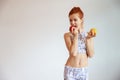 Caucasian woman in black and white sportswear holding apple and orange with undesirable face on white wall background