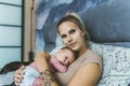 Caucasian woman with blond hair lying in bed cuddling her newborn baby resting on her chest. Proud mother looking into Royalty Free Stock Photo