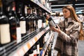 Caucasian woman chooses a bottle of wine in a grocery shop. Buying alcohol at supermarket. Royalty Free Stock Photo