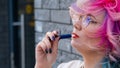 Caucasian woman with colored hair smokes an electronic cigarette. Royalty Free Stock Photo