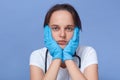 Caucasian woman doctor sitting against blue wall, having exhausted facial expression after working day, young girl medical staff Royalty Free Stock Photo