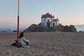 Caucasian woman with a dog seeing the beautiful chapel on the beach Capela do Senhor da Pedra at sunset in Miramar, in Portugal