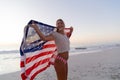 Caucasian woman holding and waving an US flag at the beach.